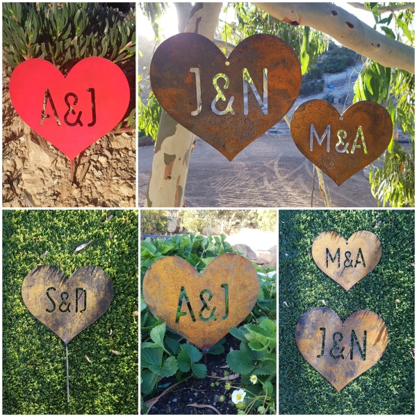 A collage of images. A red heart with the initials "A & J' staked in a garden. Two rusty hearts with the initials 'J&N' and 'M&A' hanging in a gum tree. A small rusty heart with the initials 'S&D' with a stake lying on artificial grass. A rusty heart with the initials 'A&J' staked in a strawberry bed. Two rusty hearts of different sizes - the smaller with the initials 'M&A' and the larger with the initials 'J&N' lying on a backing of artificial grass.