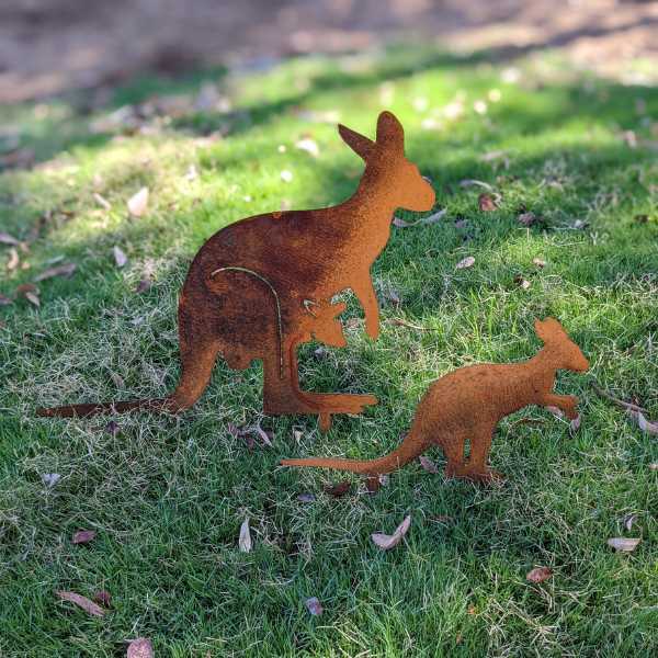 A family of 2 rusty metal kangaroos staked on lawn in a backyard. There are 2 separate metal cutouts: one kangaroo with a joey in her pouch, and a small joey.