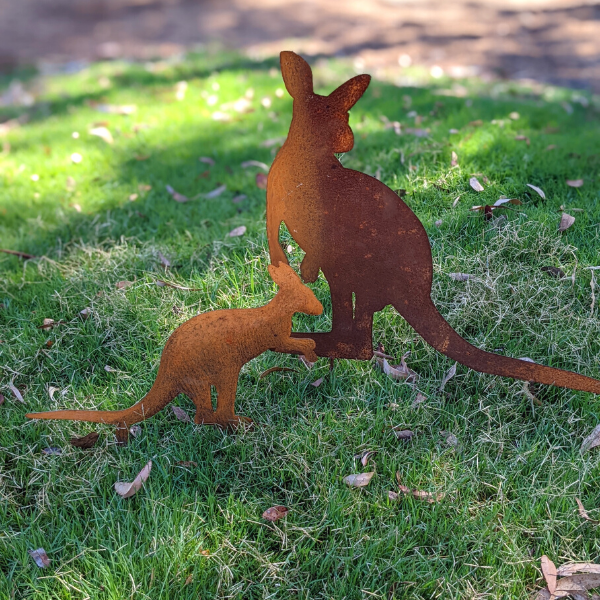 A family of 2 rusty metal kangaroos staked on lawn in a backyard. There are 2 separate metal cutouts: one adult kangaroo, and a small joey.