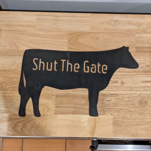 Image is a metal sign the silhouette of an Angas Cow with the words Shut the Gate.