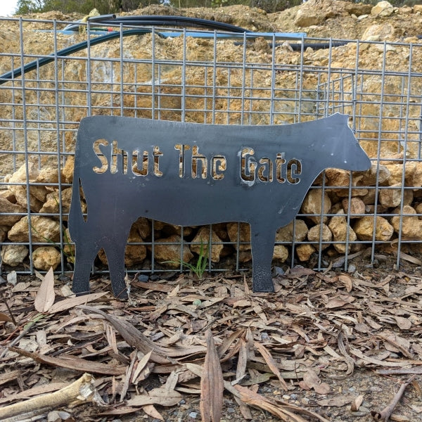 Image is a metal sign the silhouette of an Angas Cow with the words Shut the Gate. 