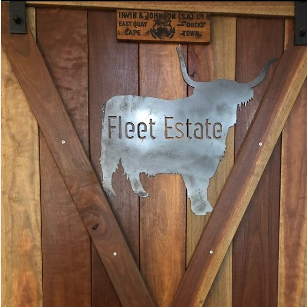 Image is a metal sign the silhouette of an Highland Cow with the words Fleet Estate. mounted to a wood panel door.